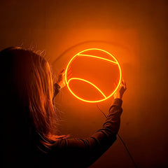 Person holding a round orange tennis ball neon light against a dark background