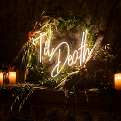 Neon sign with 'Til Death' surrounded by foliage and candles in a dark setting