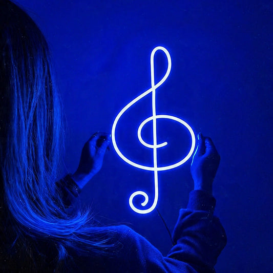 Person holding a neon blue treble clef symbol against a dark background