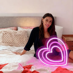 Woman holding a neon heart-shaped light on a bed