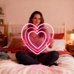Woman holding a neon pink heart shape in a bedroom setting