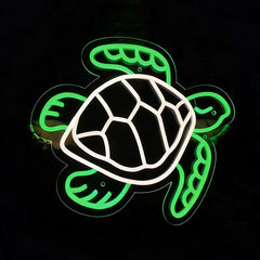 A neon-style turtle sign with a glowing green outline and a white shell, photographed against a black background.
