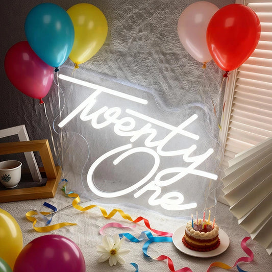 Neon sign reading 'Twenty One' with colorful balloons and a small cake.
