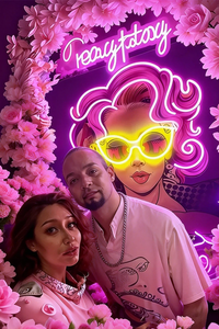 Two people posing in front of a vibrant, neon-lit poster with floral elements and 'everystory' branding.