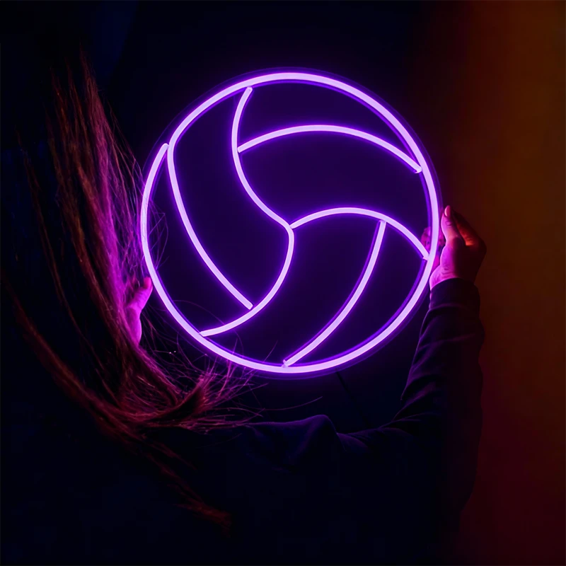Person holding a glowing purple volleyball neon sign against a dark background