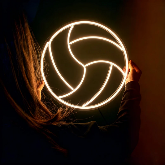 Person holding a glowing warm white volleyball neon sign against a dark background