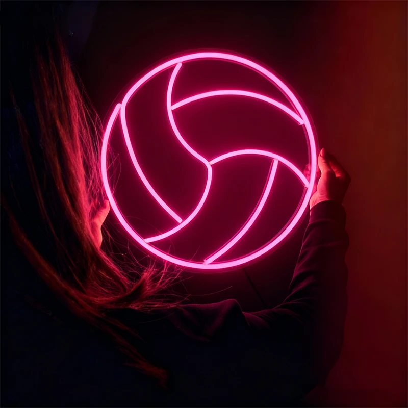 Person holding a glowing hot pink volleyball neon sign against a dark background