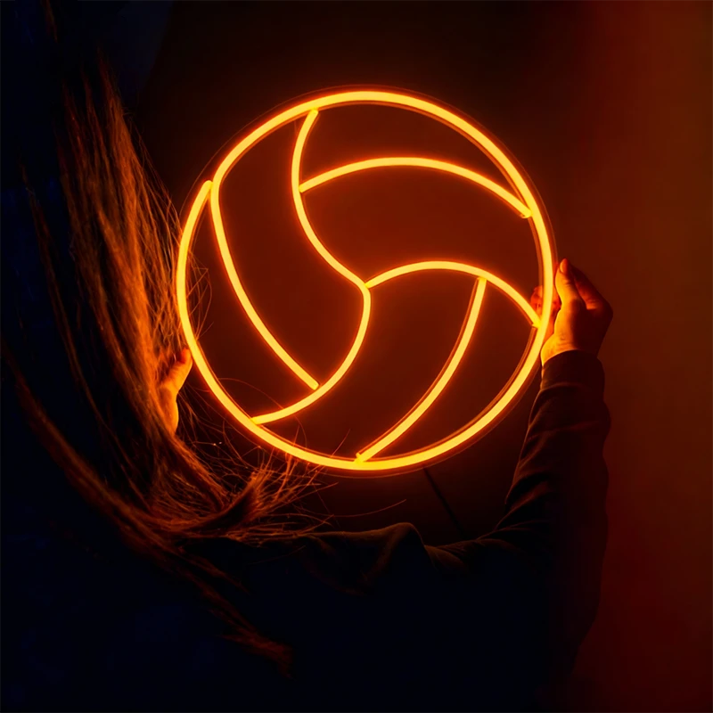 Person holding a glowing orange color volleyball neon sign against a dark background