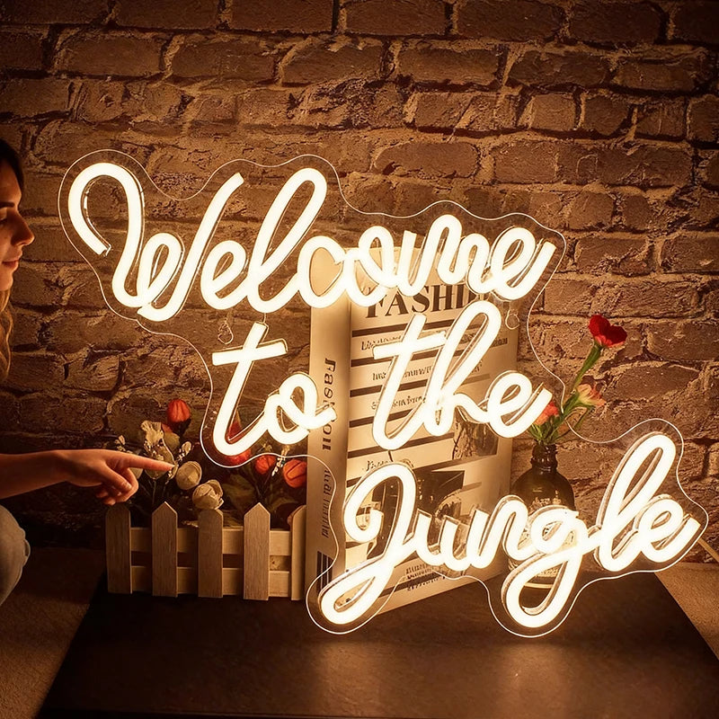 Woman holding a drink in front of a 'Welcome to the Jungle' neon sign at a festival.