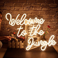 Woman holding a drink in front of a 'Welcome to the Jungle' neon sign at a festival.