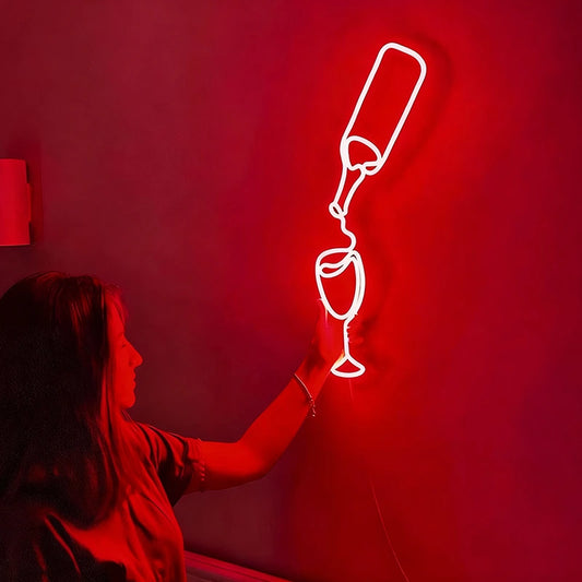 Person interacting with a neon light shaped like a champagne bottle and glass on a red wall.