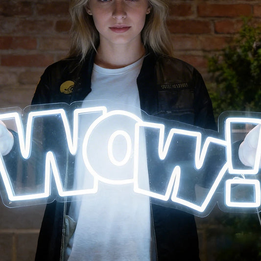 Person holding a neon sign with the word 'WOW!' in front of a brick wall.