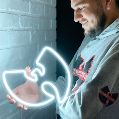 Man holding a white neon sign shaped like a Wu-Tang Clan logo in front of a brick wall.