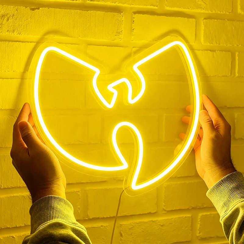 Neon sign shaped like a lemon yellow Wu-Tang Clan logo held by two hands against a brick wall.