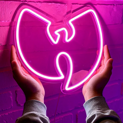 Neon hot pink 'Wu-Tang' logo held by hands against a brick wall.