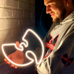 Person holding a neon light shaped like a Wu-Tang Clan logo, wearing a hoodie with a logo.