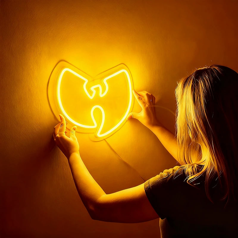Person holding a neon sign shaped like the Wu-Tang Clan logo against an orange wall.