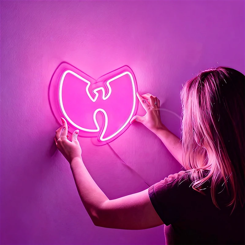 Person holding a hot pink neon Wu-Tang Clan logo against a purple background