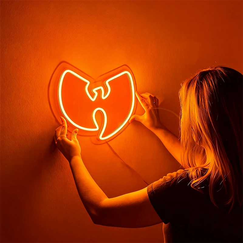 Person holding a neon sign shaped like the Wu-Tang Clan logo against an orange background