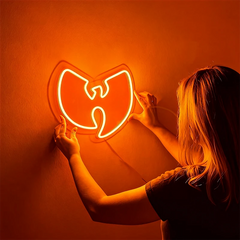Person holding a neon sign shaped like the Wu-Tang Clan logo against an orange background