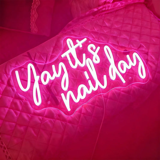 Neon sign with 'Yay it's nail day' text on a pink quilted surface