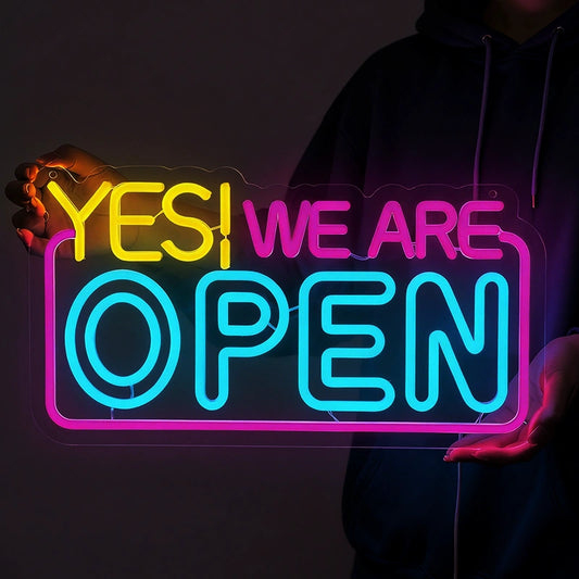 Neon sign that reads 'YES! WE ARE OPEN' held by a person against a dark background