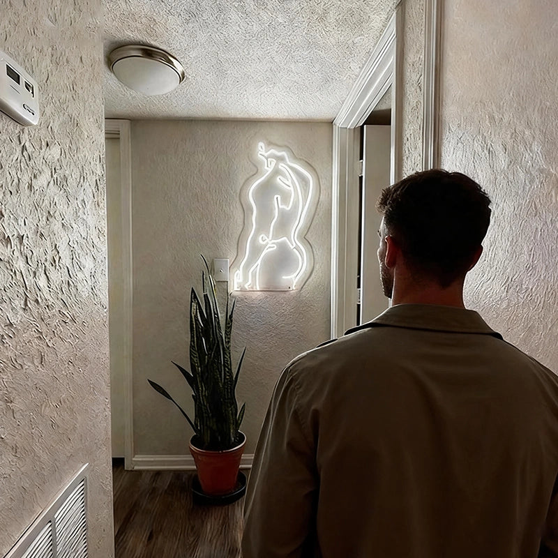 Man standing in a room with a male's body neon sign on the wall.