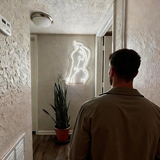 Man standing in a room with a male's body neon sign on the wall.