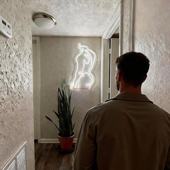 Man standing in a room with a male's body neon sign on the wall.