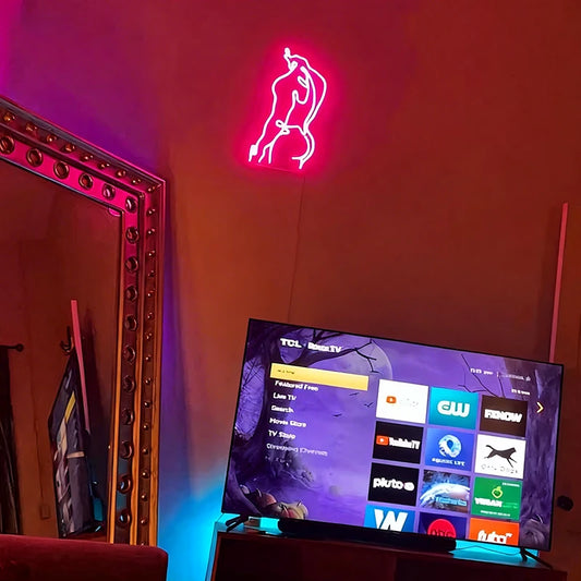Neon sign of a male's body on a dark wall with a TV displaying streaming services.