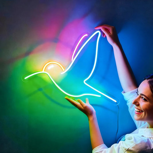 Person holding a neon light shaped like a colorful hummingbird against a drak background