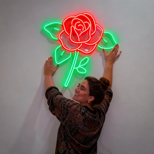 Person posing with a neon rose light fixture on a plain wall