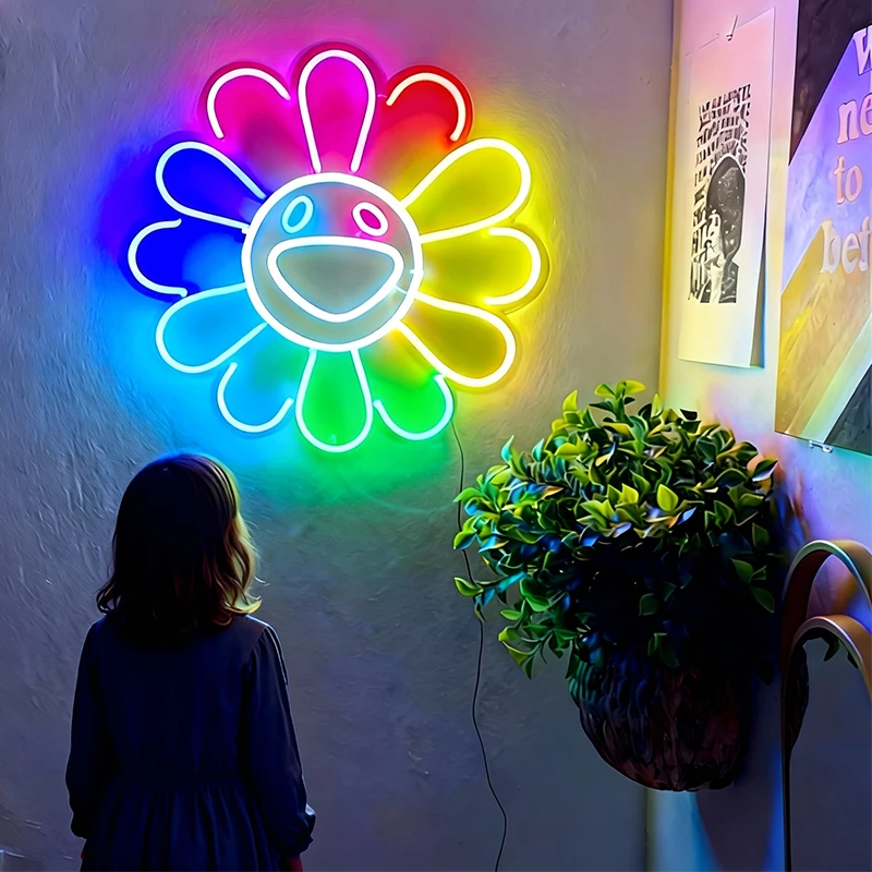 Neon flower-shaped light fixture on a wall with a person and plant in the foreground.
