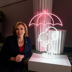 Woman sitting next to a neon sign of a dog under an umbrella
