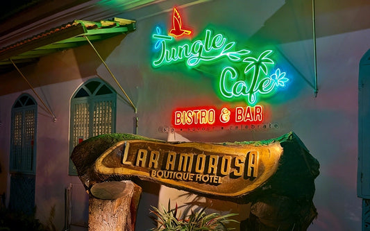 Neon sign for Jungle Cafe Bistro & Bar above a wooden sign for La Amorosa Boutique Hotel.